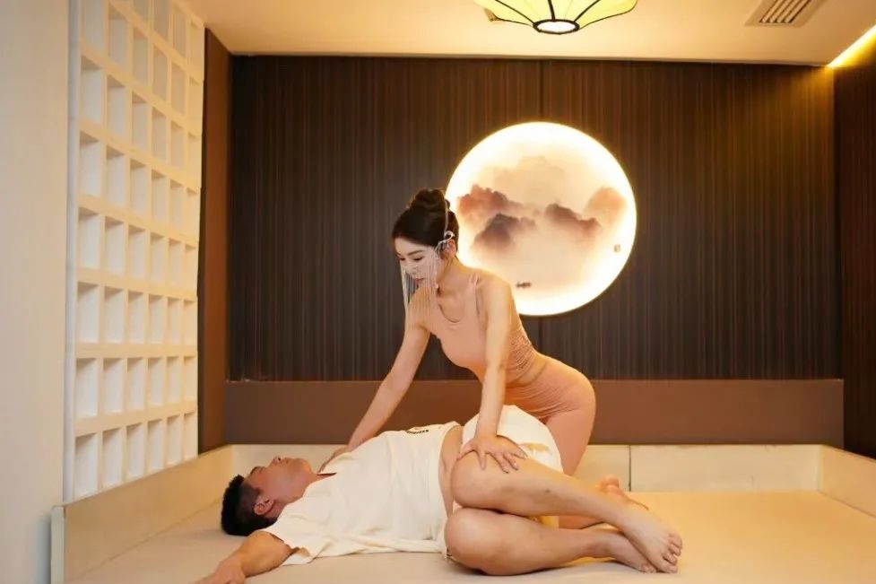 Female therapist assisting a male guest with a guided massage stretch in a warmly lit room